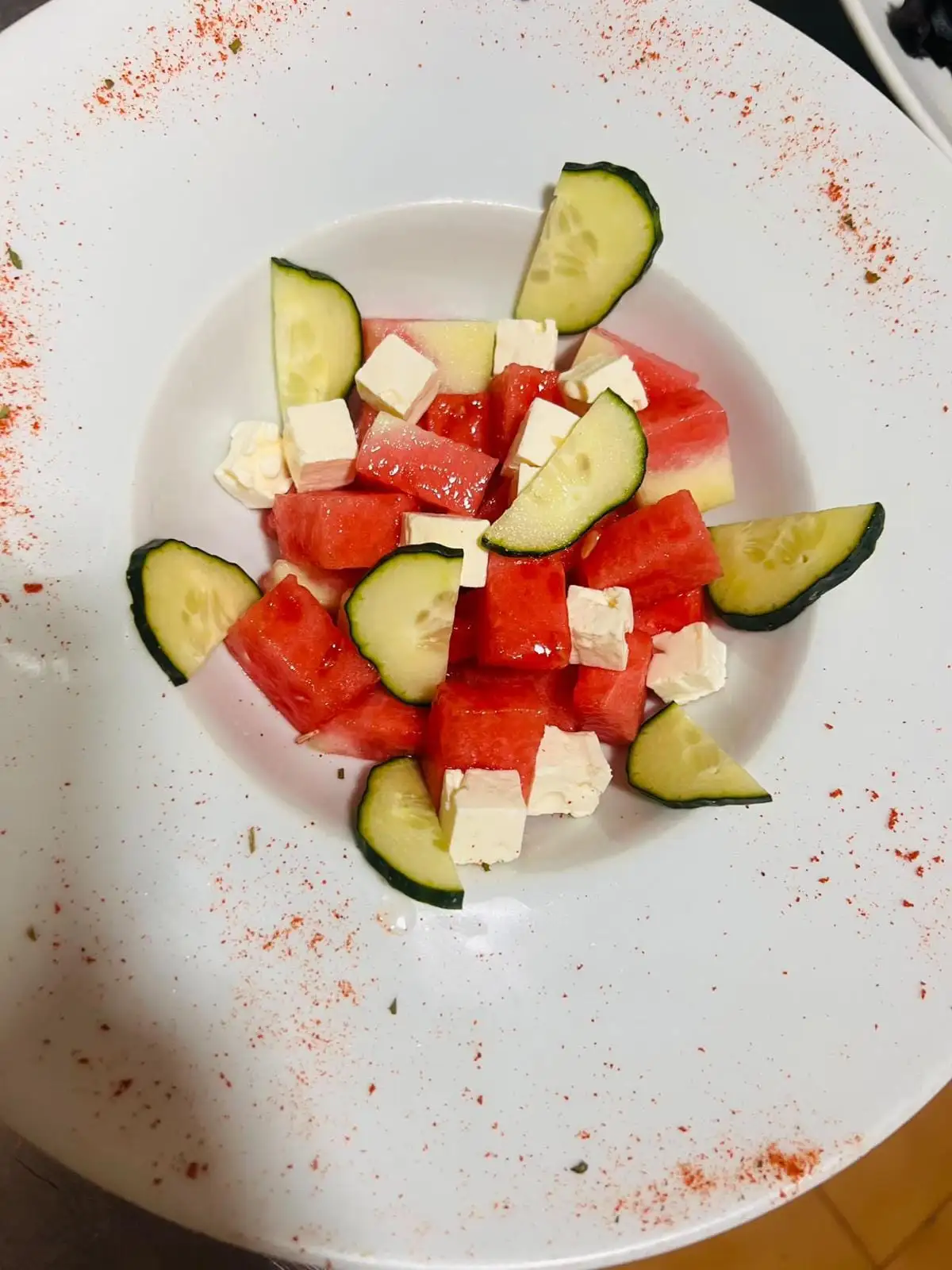 Watermelon salad with cubes of feta cheese and slices of cucumber, on a white plate.
