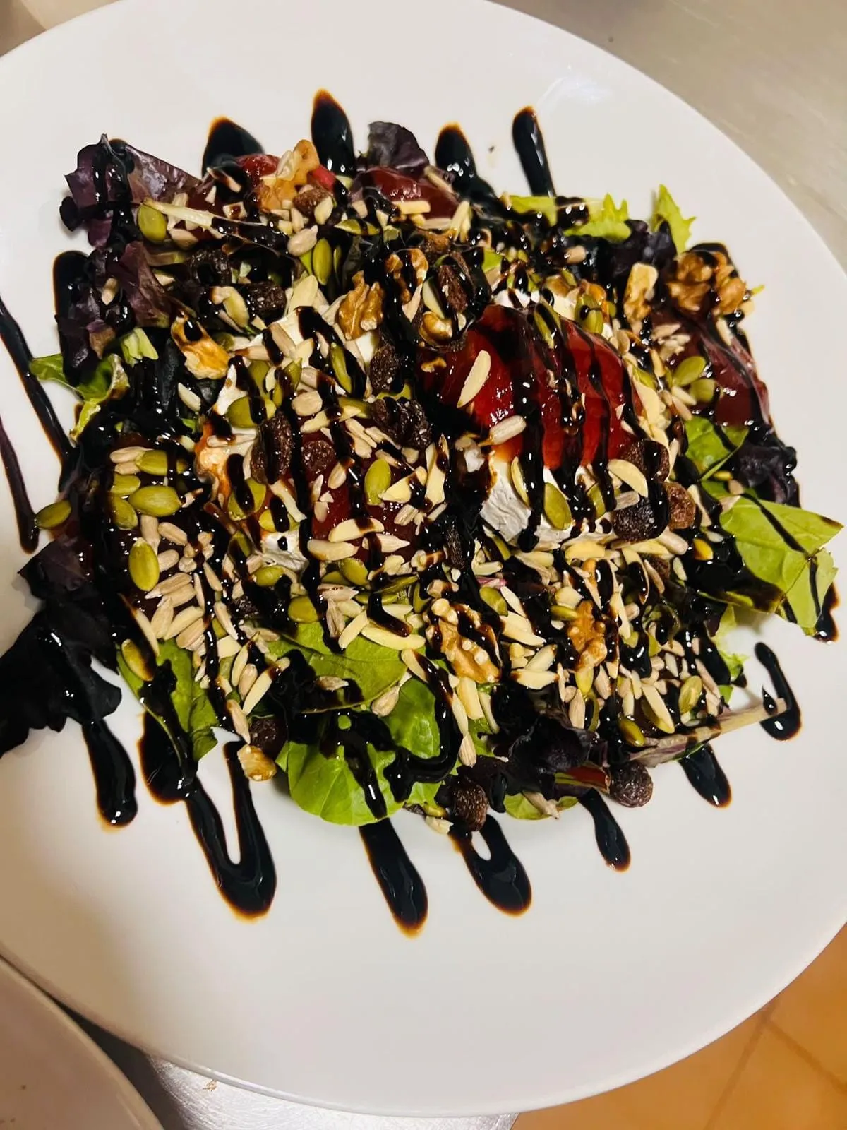 A leaf salad with rounds of goat cheese under red jam, walnuts, flaked almonds, seeds and raisins, finished with a balsamic drizzle.