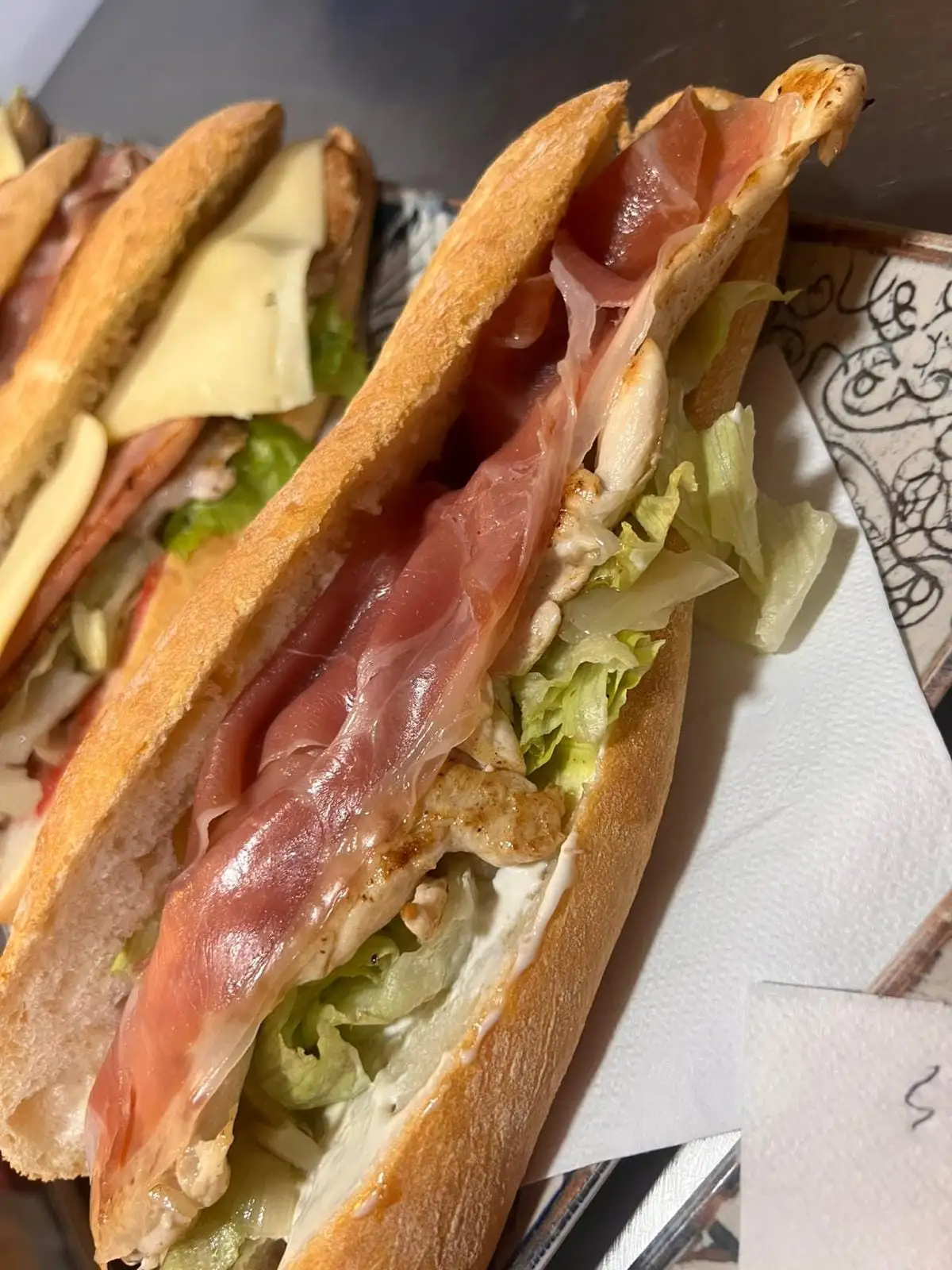 An open baguette sandwich with serrano ham, grilled fillets, lettuce and mayonnaise showing at the bread.