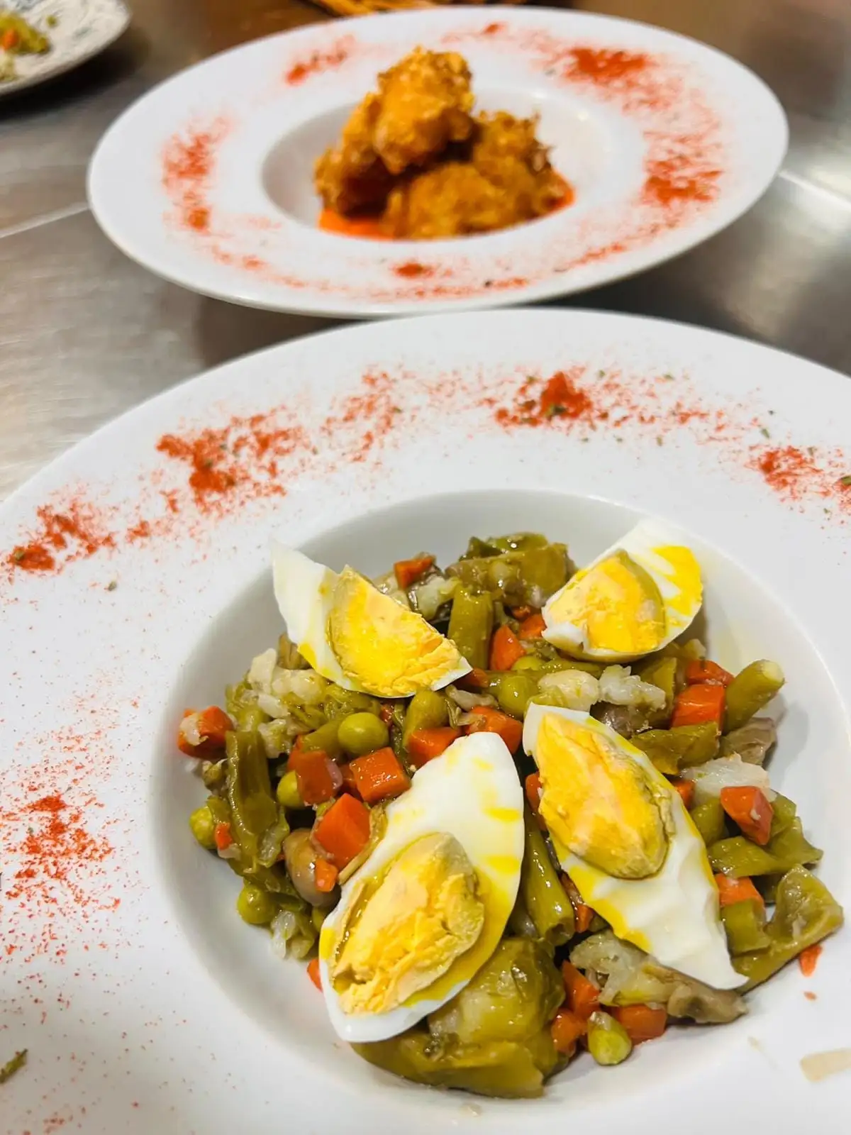 Stewed vegetables with green beans, carrot, peas and artichoke, topped with quarters of hard-boiled egg, paprika dusted around the rim.