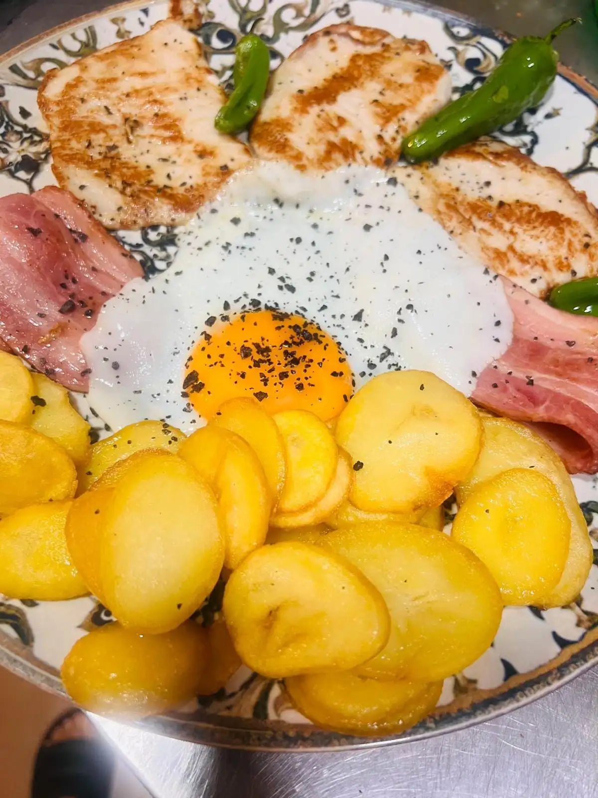 A plate with grilled fillets, rashers of bacon, a fried egg, sliced potatoes and green peppers.