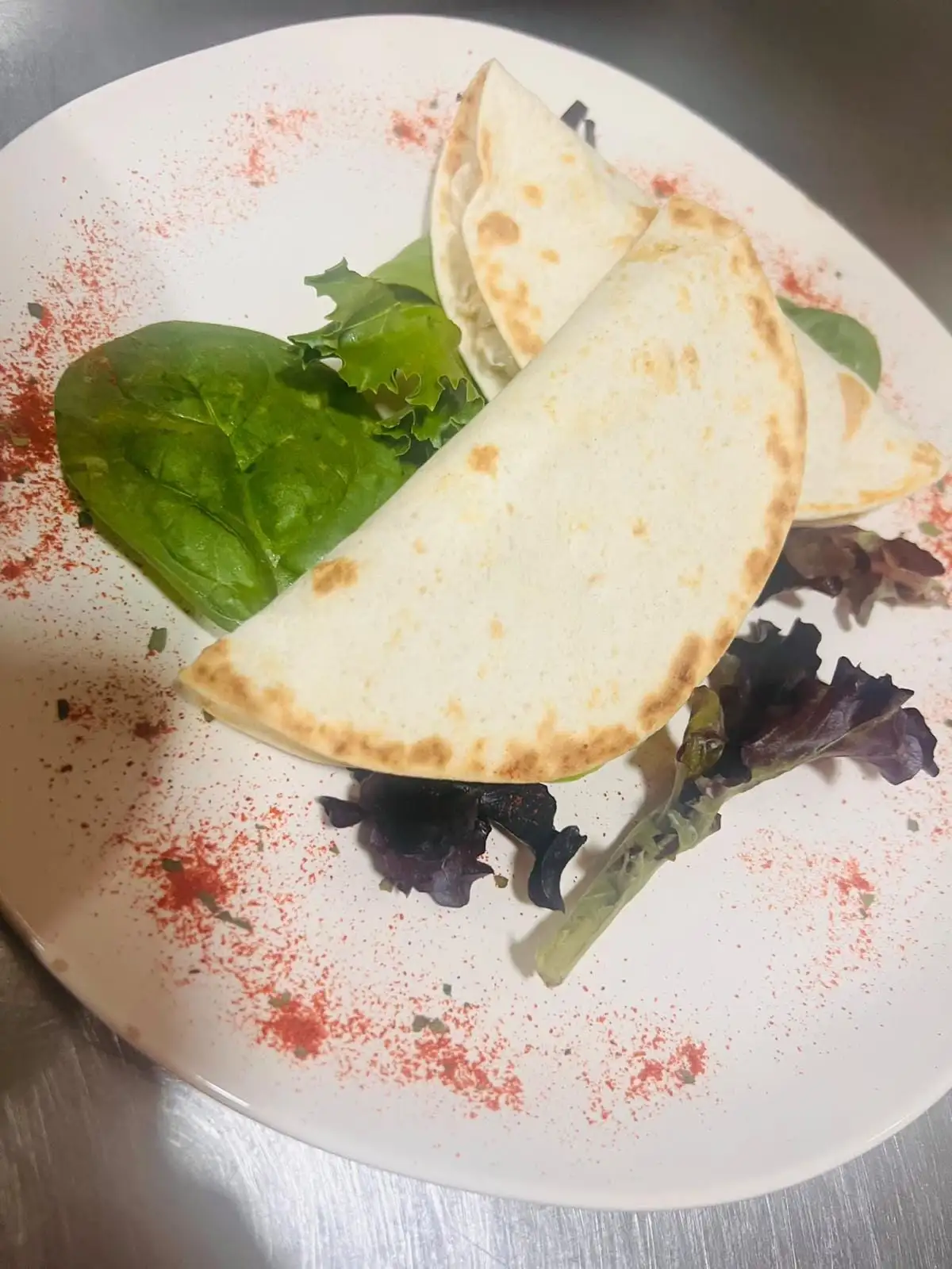 Two folded wheat tortillas, lightly toasted, on a white plate with mixed salad leaves and a dusting of paprika.