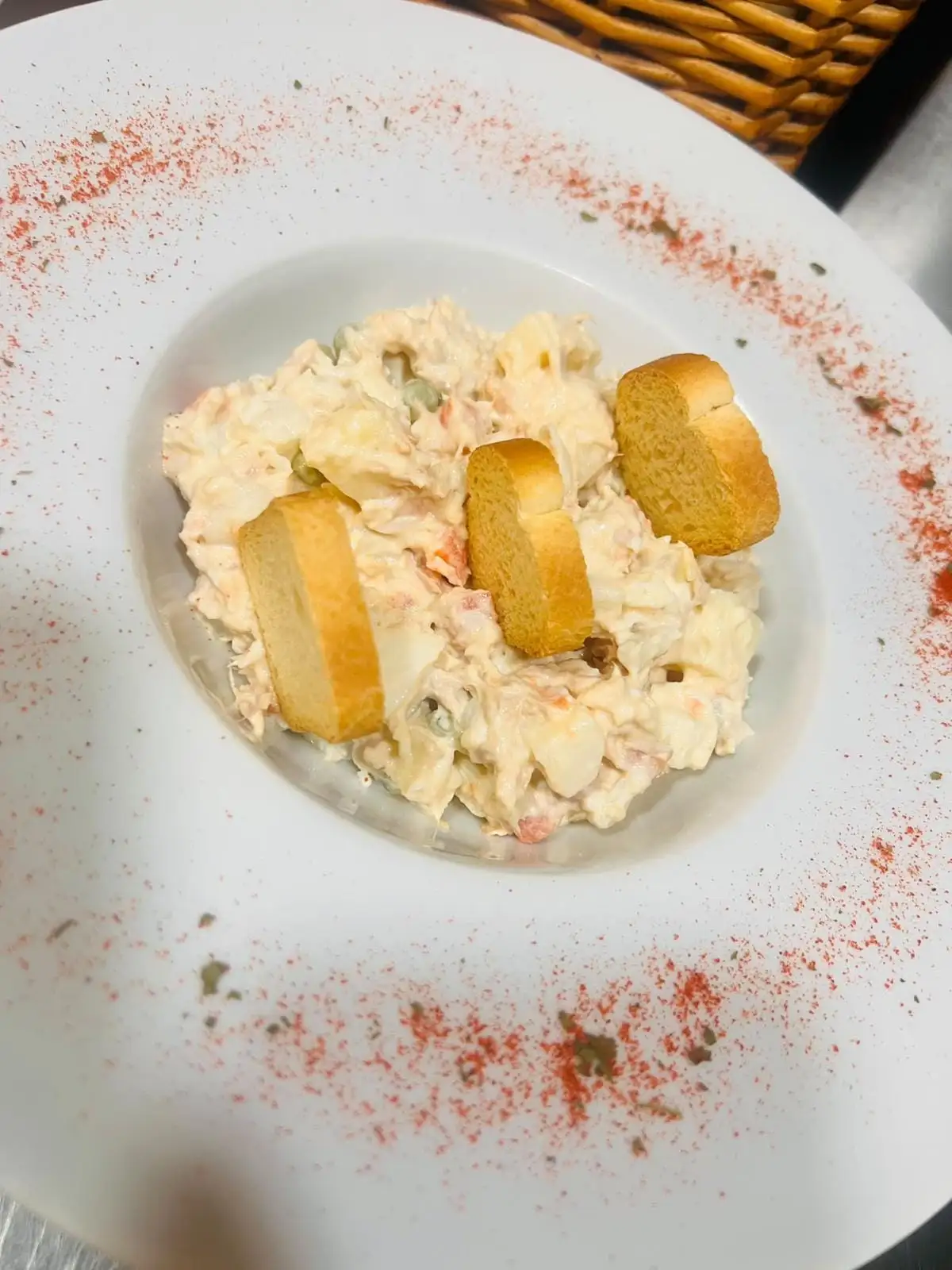 A potato salad with mayonnaise, carrot and peas in a shallow bowl, with three small slices of toast on top.