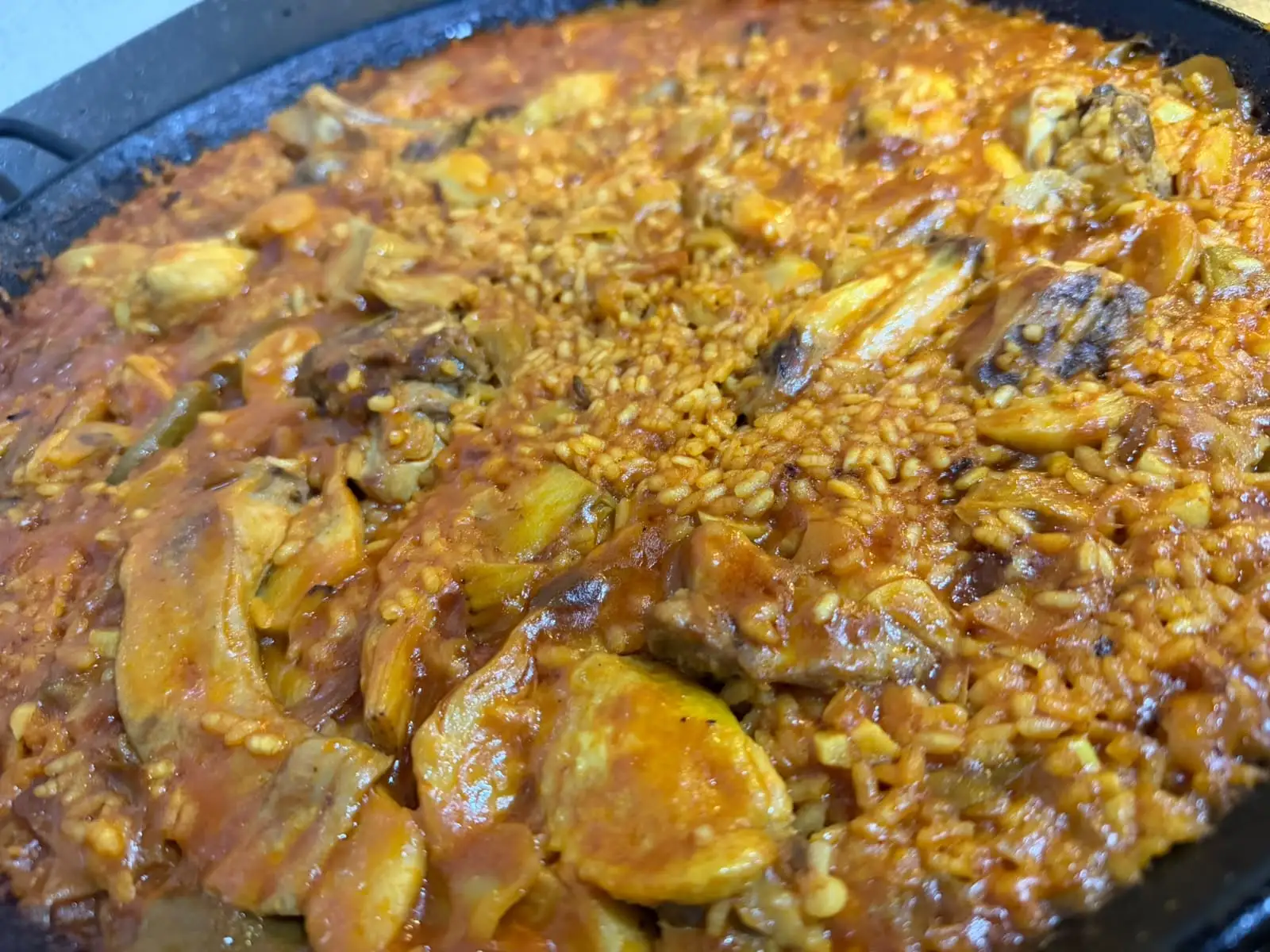Close-up of a juicy rice in the pan, with pieces of meat and artichoke among the grains.