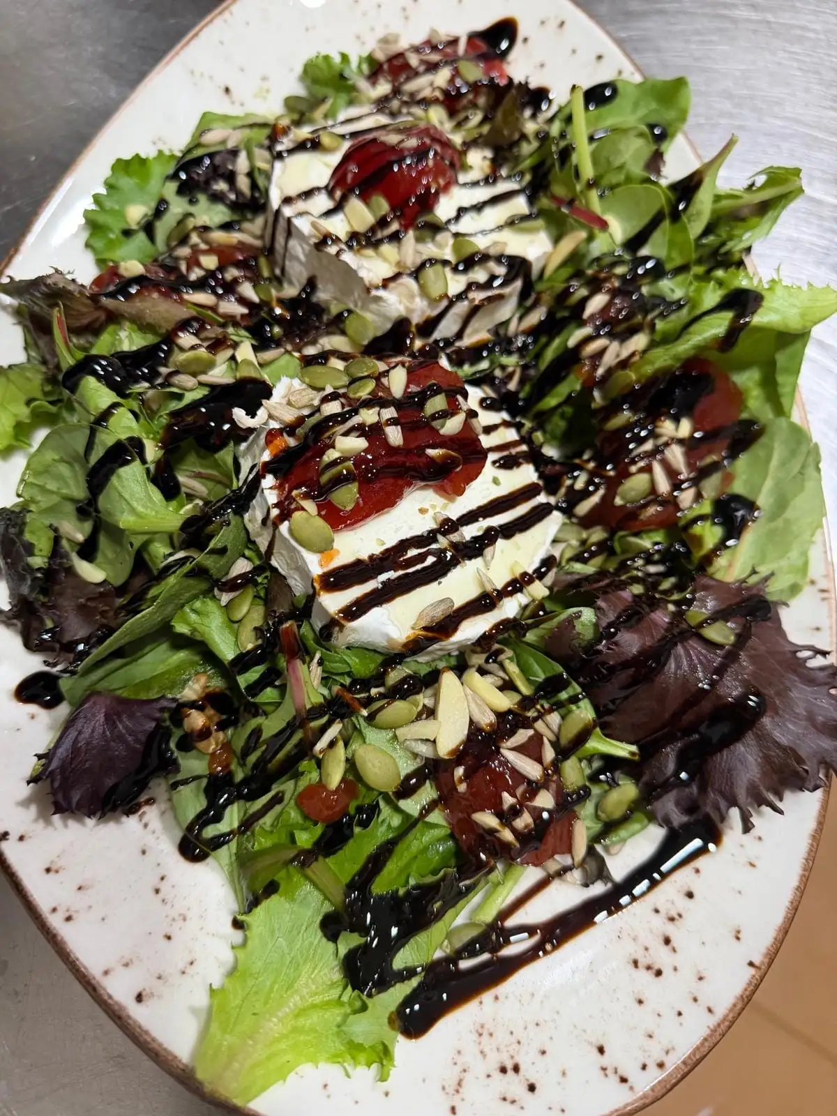 Rounds of goat cheese with tomato confit on mixed leaves, with seeds, flaked almonds and a drizzle of balsamic reduction.