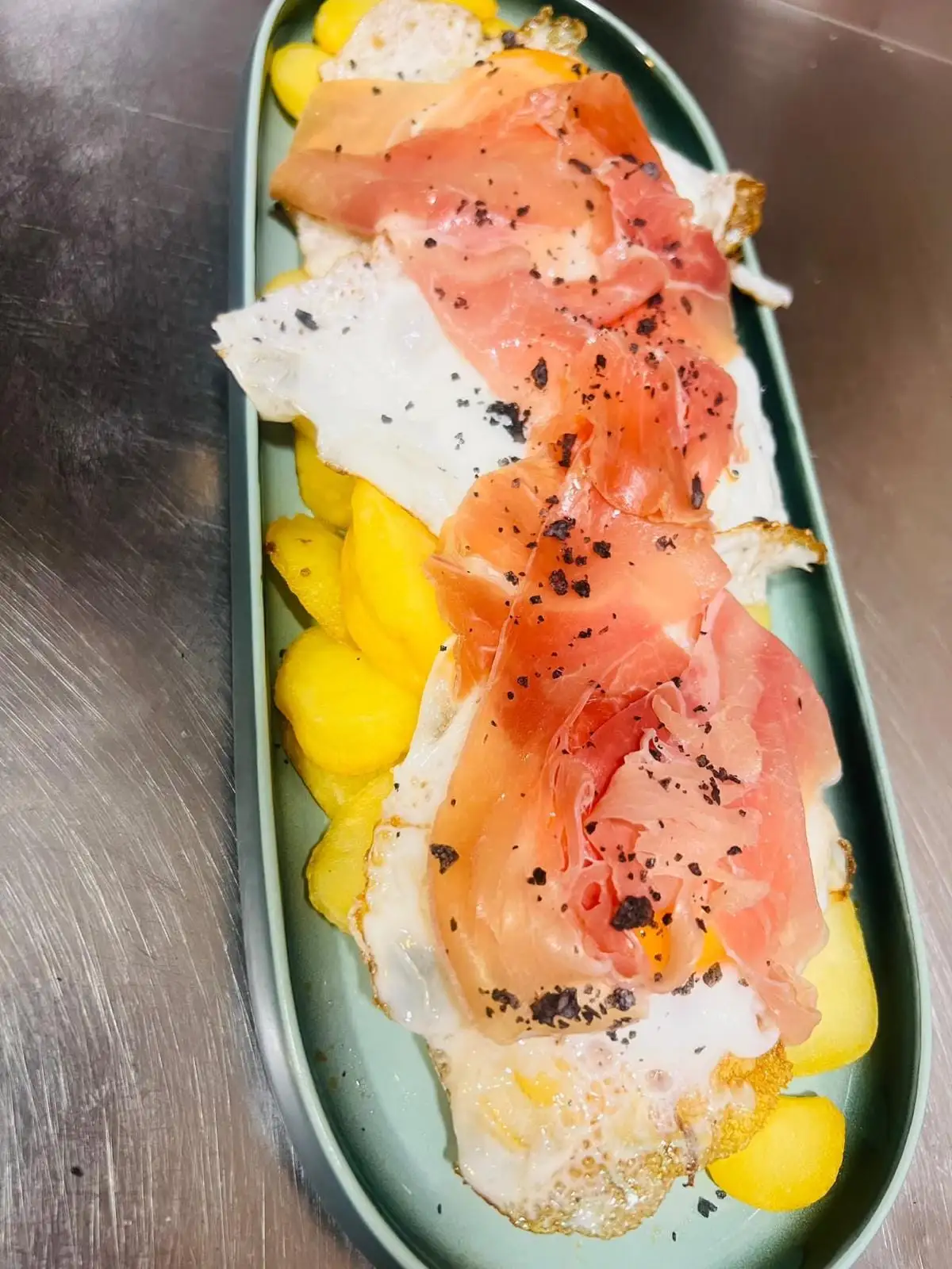 Fried eggs with slices of serrano ham over fried potatoes, served on an oval dish and sprinkled with black pepper.