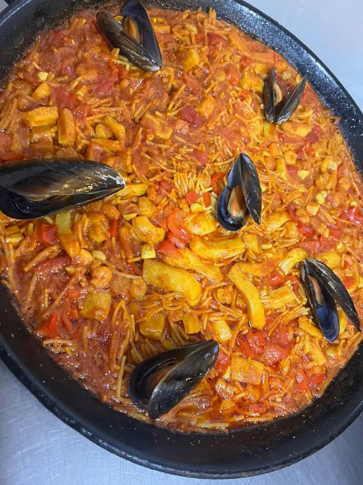 Fideuá in the pan, with open mussels and strips of red pepper among the noodles.