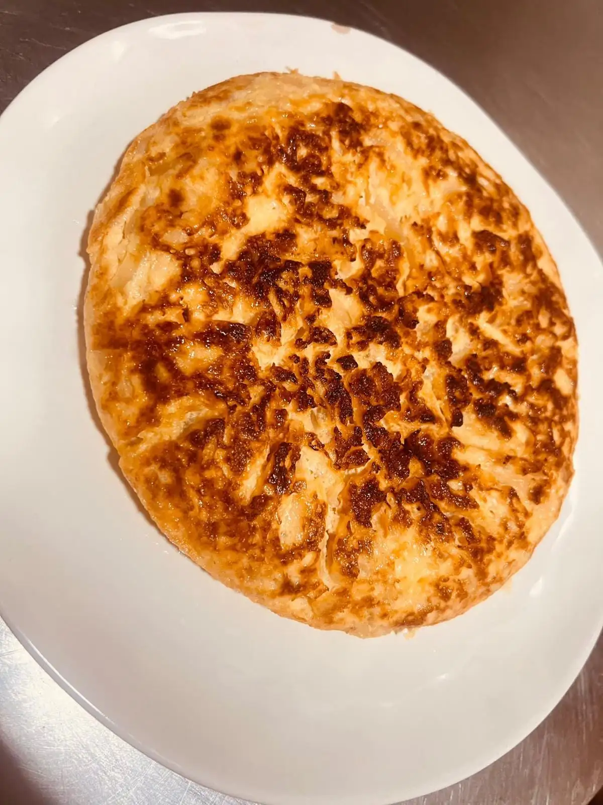 A whole, well-browned potato omelette served on a white oval plate.