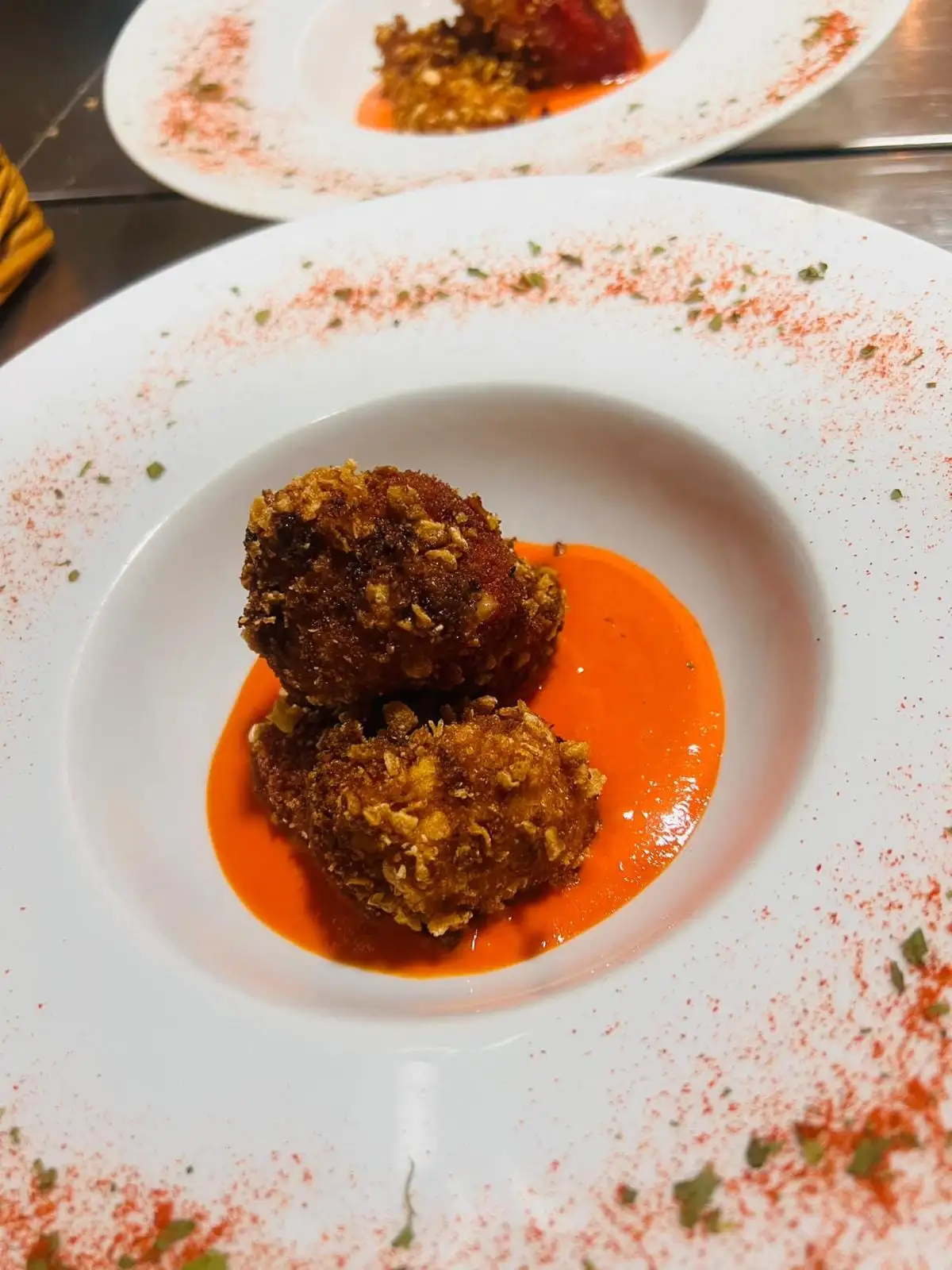 Two croquettes in a crunchy coating on a pool of orange sauce, in a deep plate with paprika dusted around the rim.