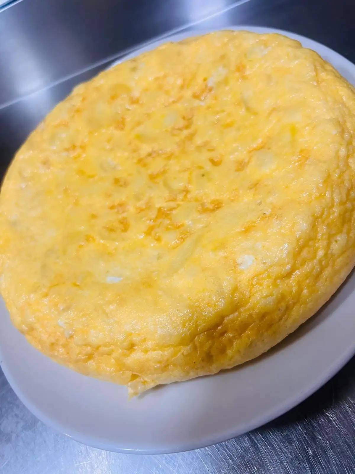A tall, softly set potato omelette served whole on a white plate.