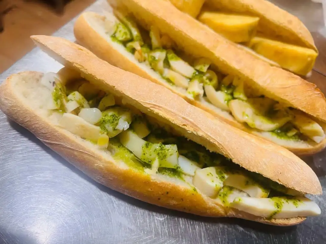 Two open baguette sandwiches filled with chopped cuttlefish in green garlic and parsley sauce, with fried potatoes behind.