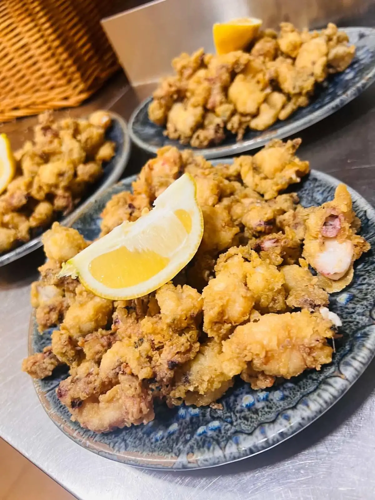 Three speckled blue plates of battered fried squid, each topped with a wedge of lemon.