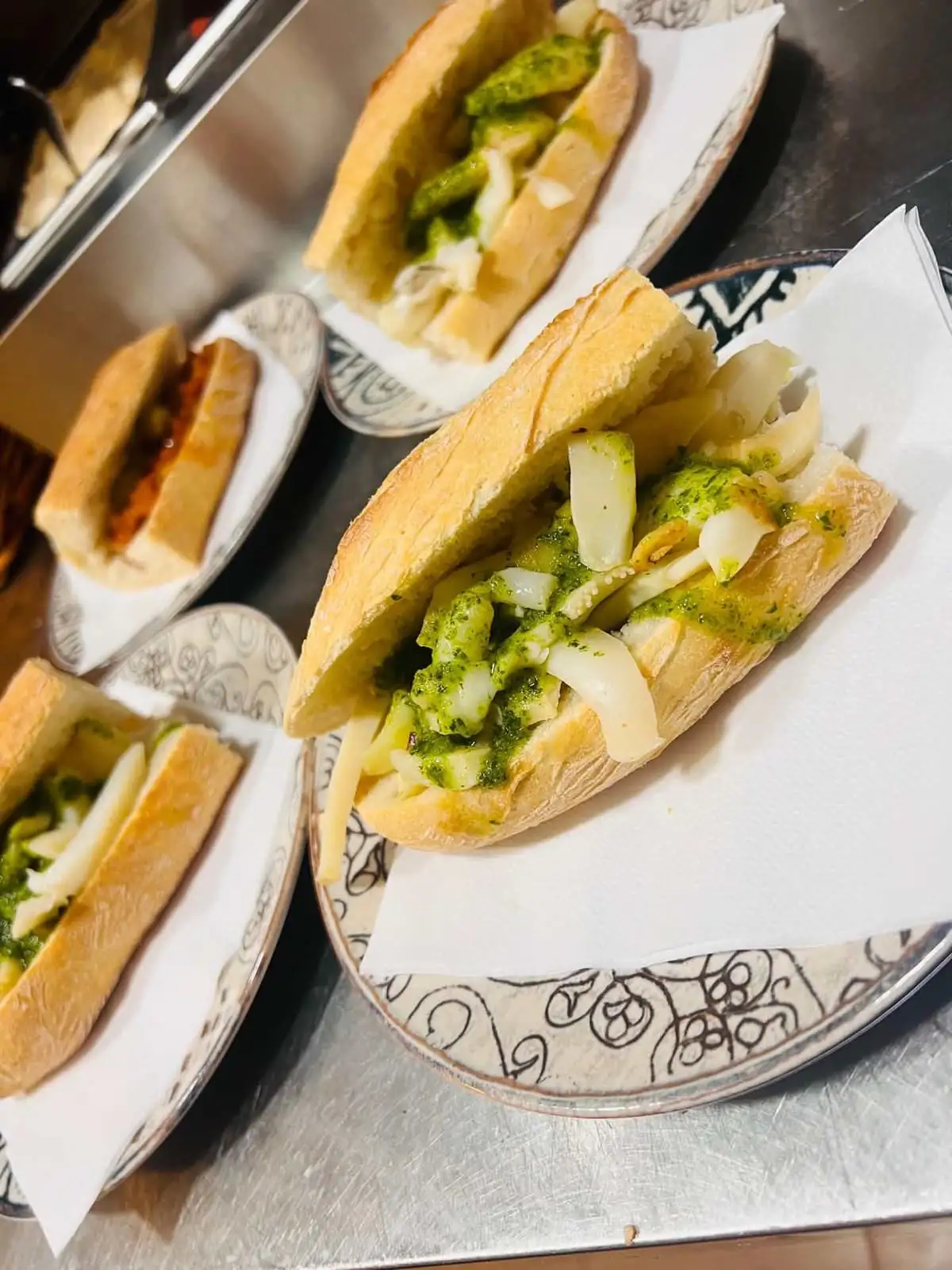 Several cuttlefish sandwiches in green parsley sauce, served on napkins on patterned ceramic plates.
