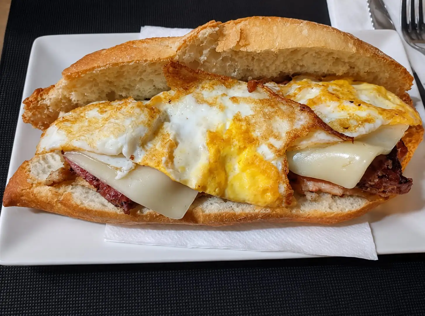 Open sandwich on a white plate, with grilled meat, melted cheese and a fried egg on top.