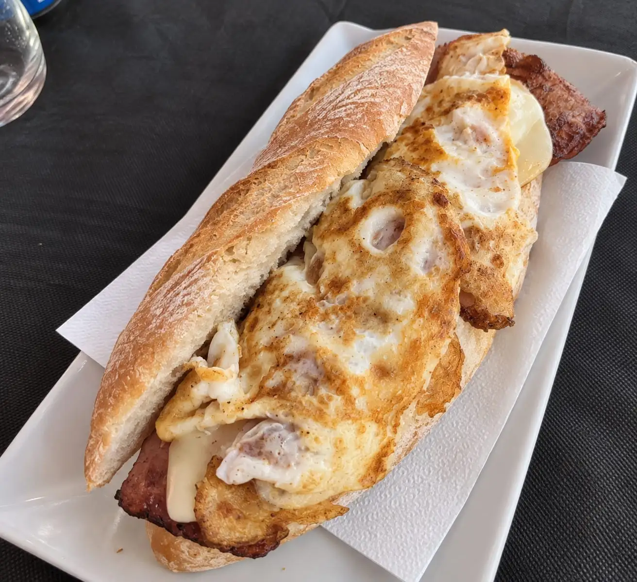 Open roll with omelette, bacon and melted cheese, served on a white plate.