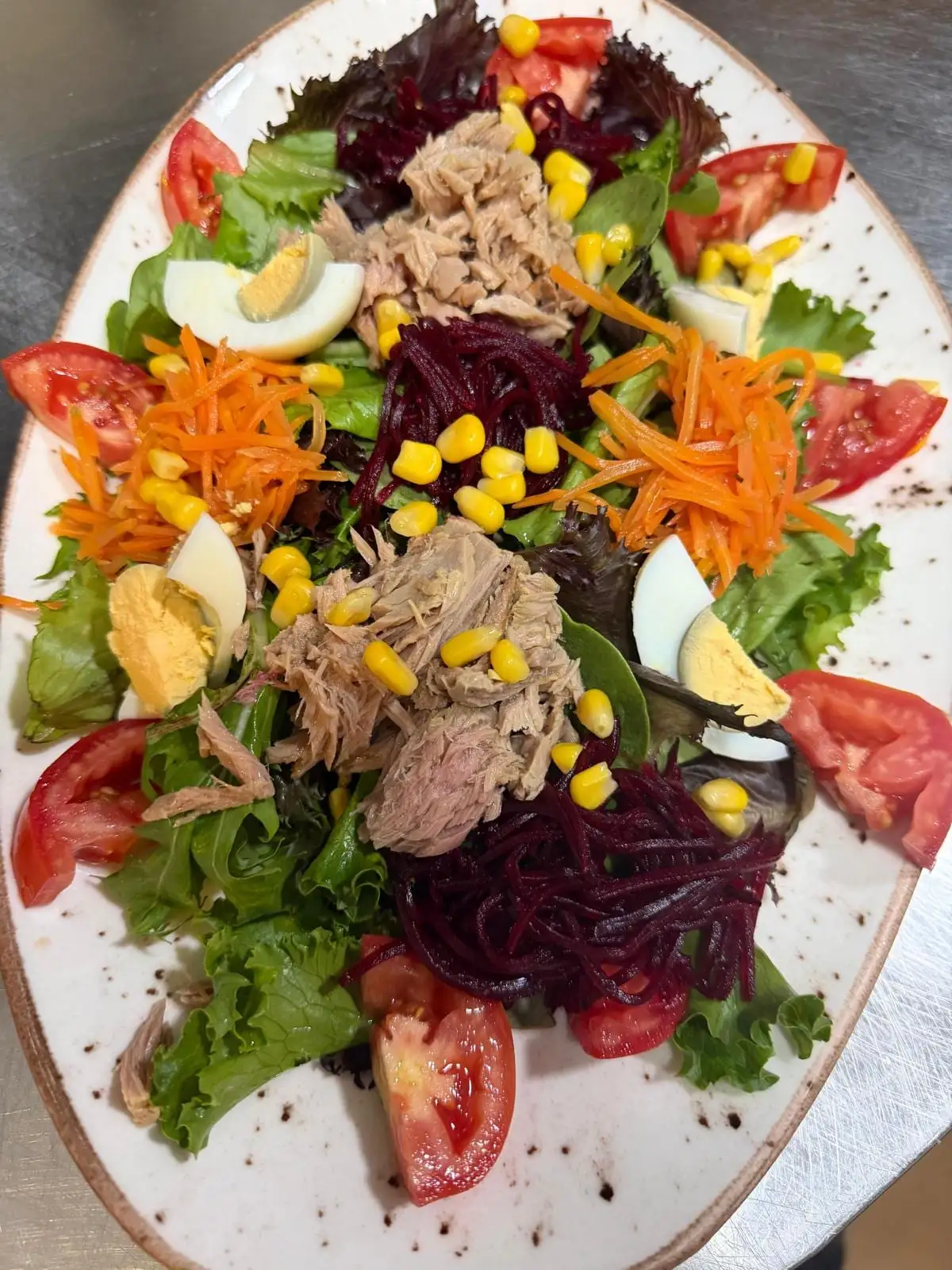 A mixed salad on an oval plate: lettuce, tomato, grated carrot and beetroot, sweetcorn, hard-boiled egg and tuna.