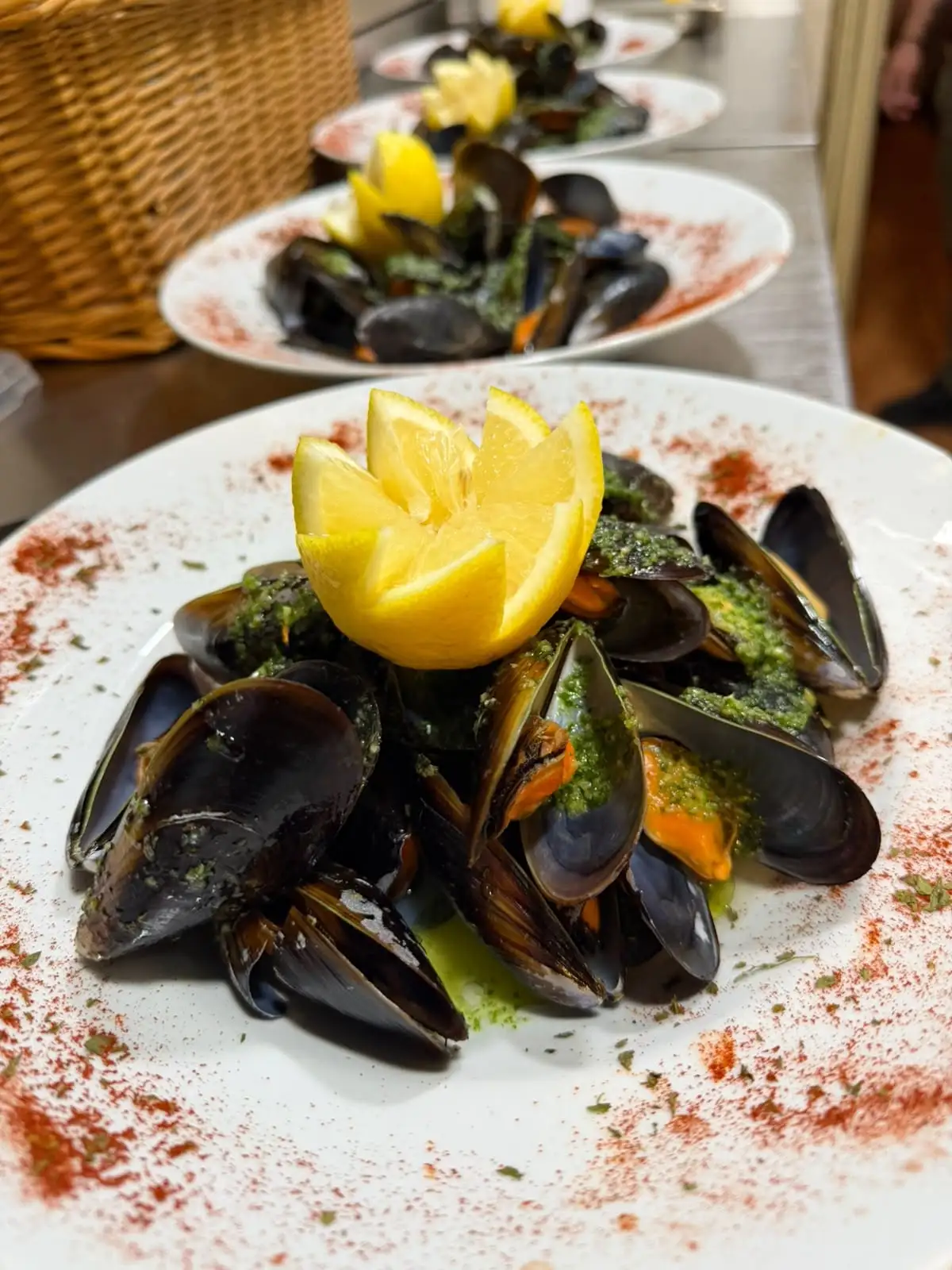A plate of steamed mussels with green sauce and a carved lemon on top.