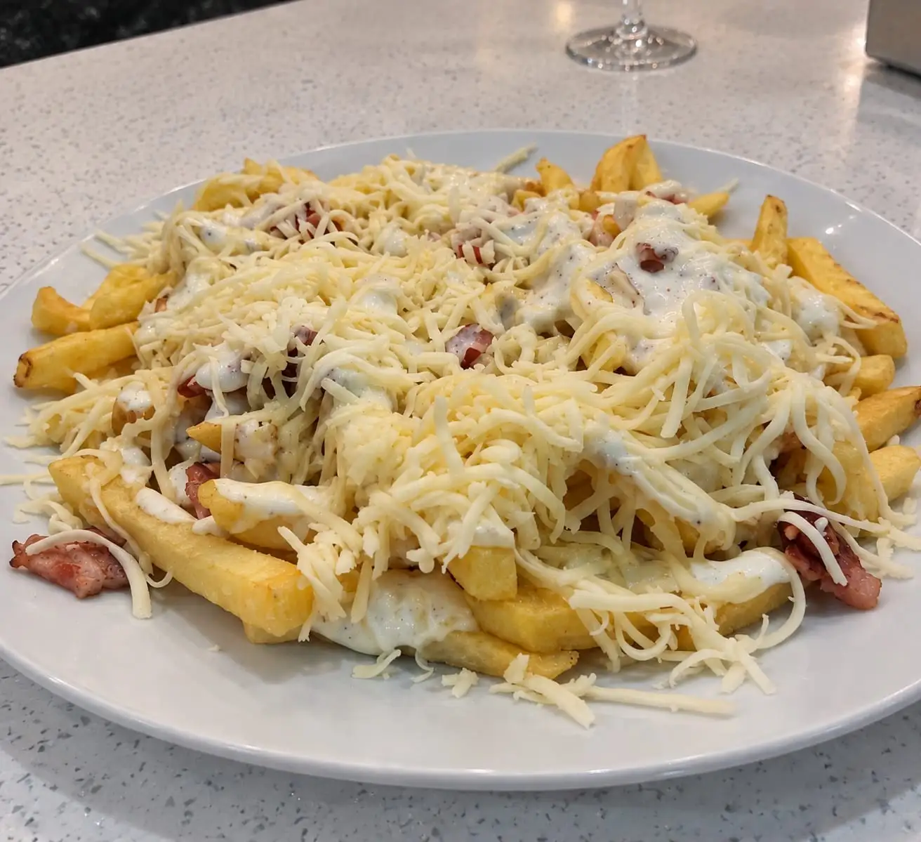 Dish of chips with grated cheese, bacon and sauce on top.