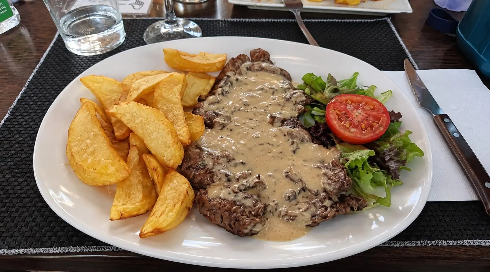 Combination plate: steak with mushroom sauce, potato wedges and a salad with tomato.