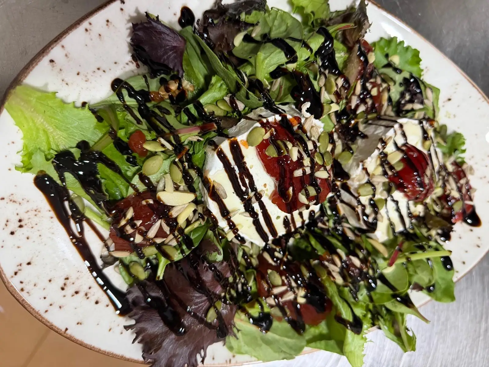 Goat cheese salad on mixed leaves, with tomato jam, seeds, flaked almonds and a balsamic reduction.