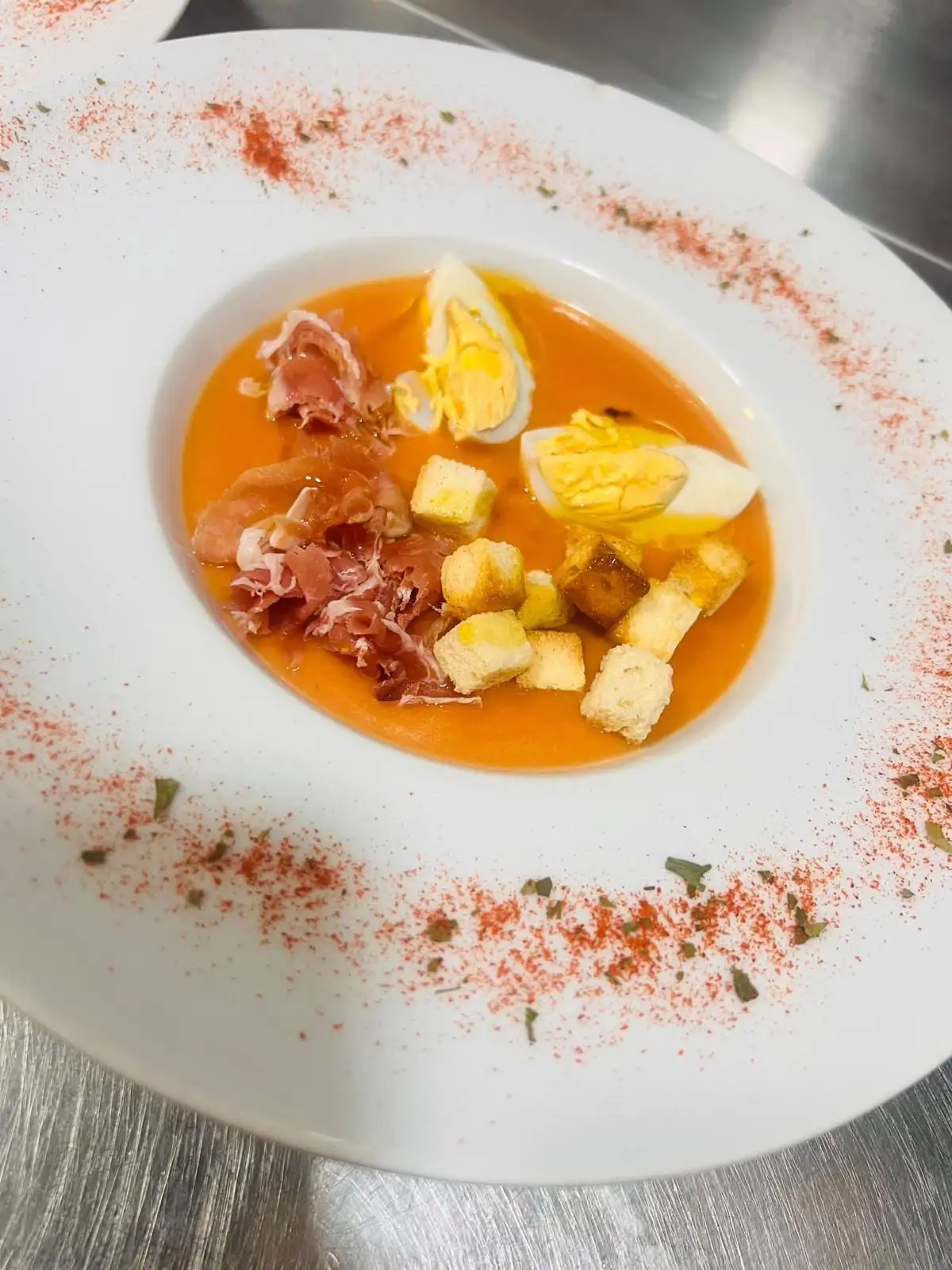 Salmorejo in a deep plate with chopped hard-boiled egg, shavings of serrano ham and croutons, paprika dusted around the rim.