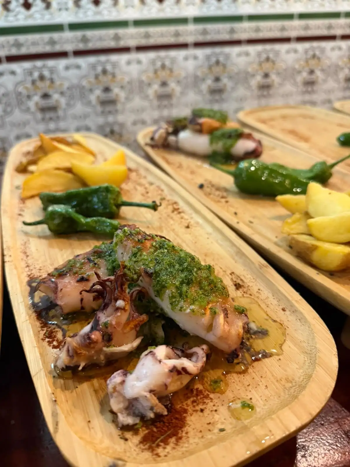 Grilled cuttlefish with a green garlic and parsley sauce, with Padrón peppers and potatoes beside it.