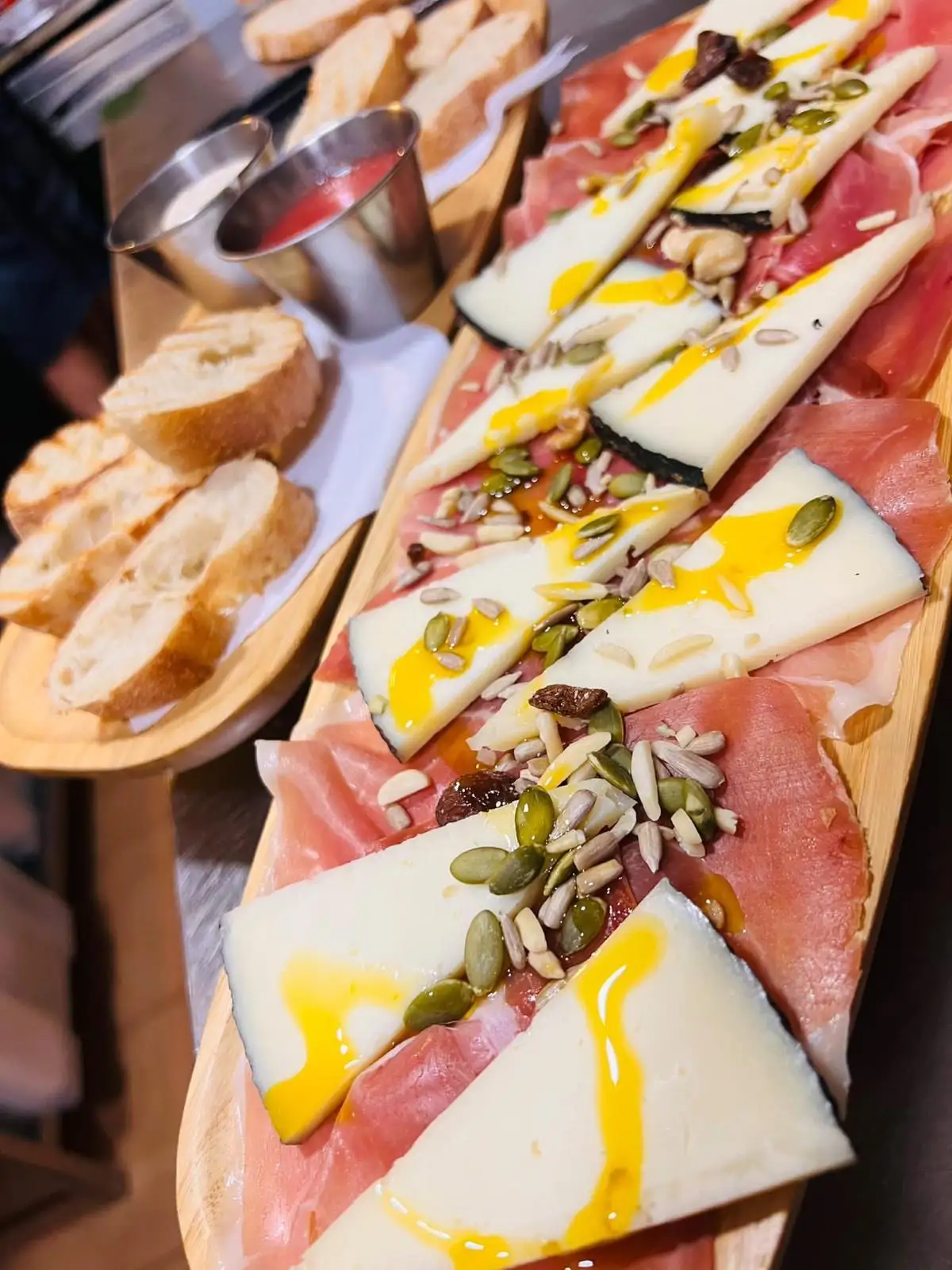 A board of serrano ham and cured cheese with nuts, a drizzle of oil and toasted bread beside it.