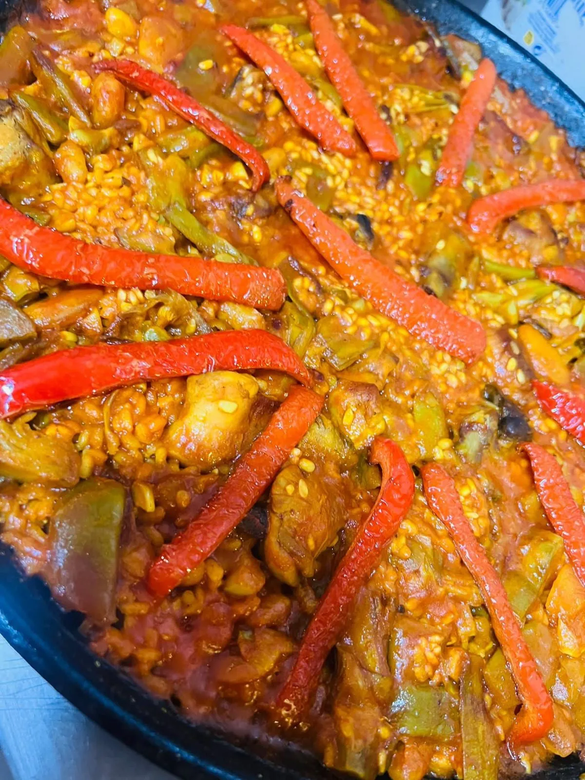 A vegetable rice in the pan: green beans, artichoke, butter beans and strips of roasted red pepper over the rice.